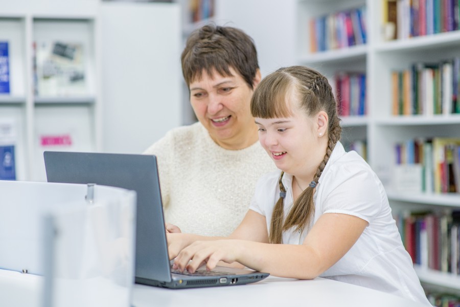 Girl and woman working on a laptop in a library