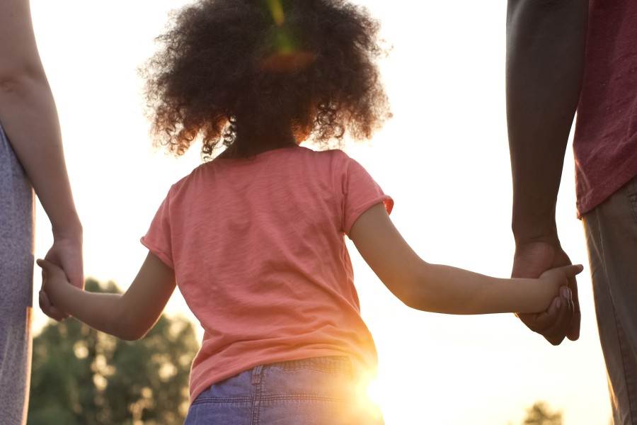 Back view of a small girl holding the hands of two adults