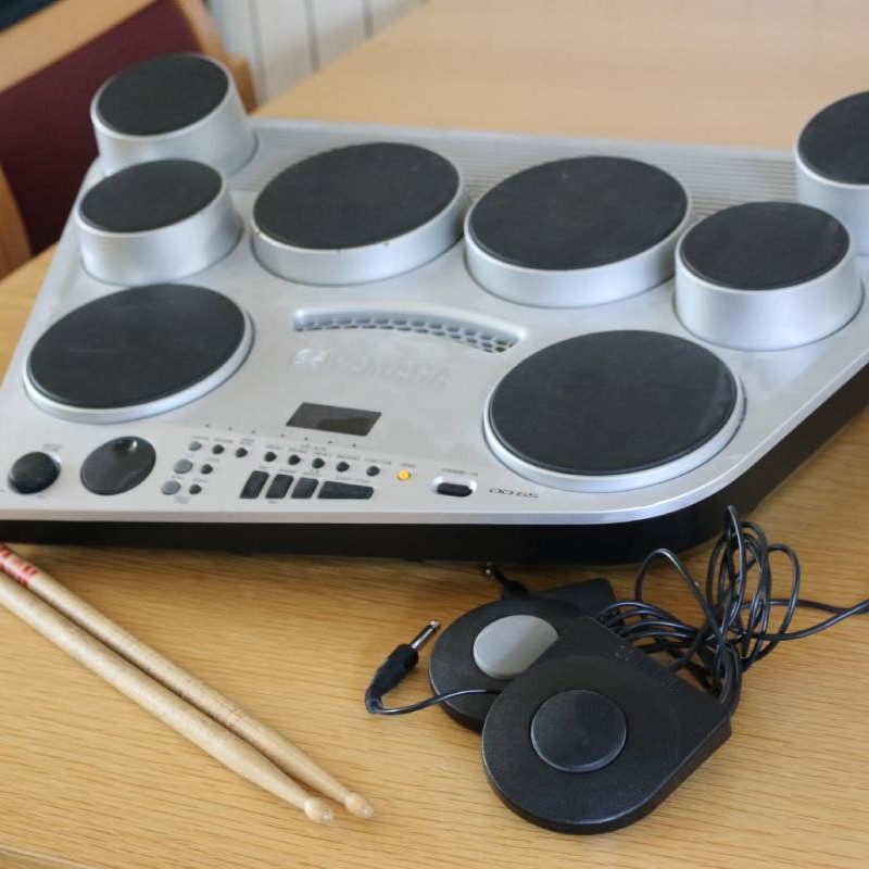 Digital drum kit on a table with foot pedals and a pair of drumsticks
