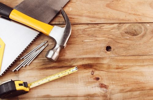 A hammer, measuring tape, and nails on a wooden surface
