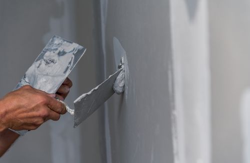 Hands holding plastering tools while working on a wall