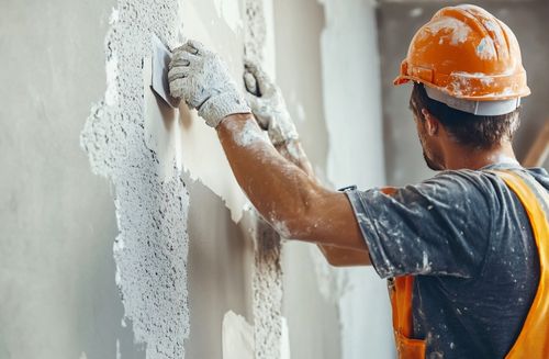 A man in a hard hat and hi-vis plastering a wall