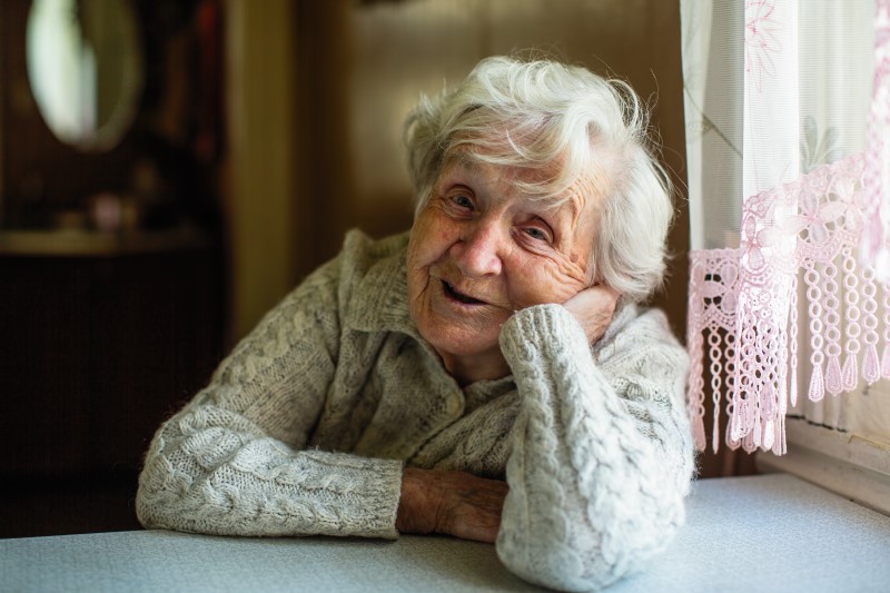 Elderly woman leans on a table smiling at the camera