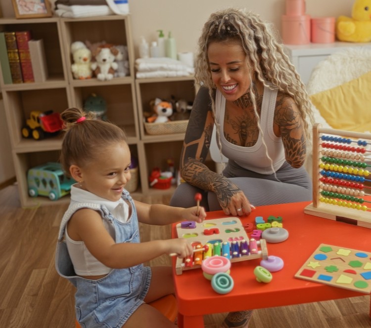 A smiling mother and child sitting at a red children's table, playing with different toys