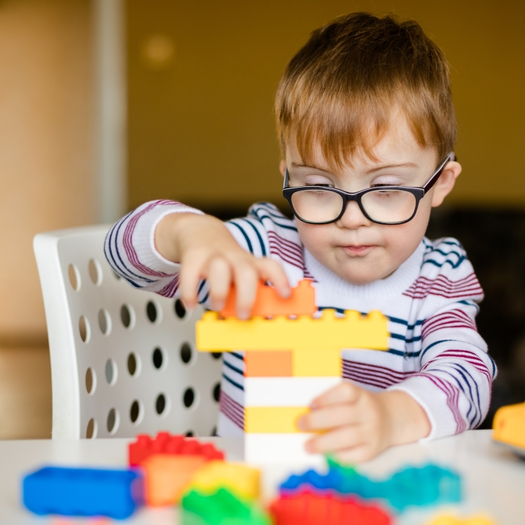 Child with glasses building a tower out of Lego