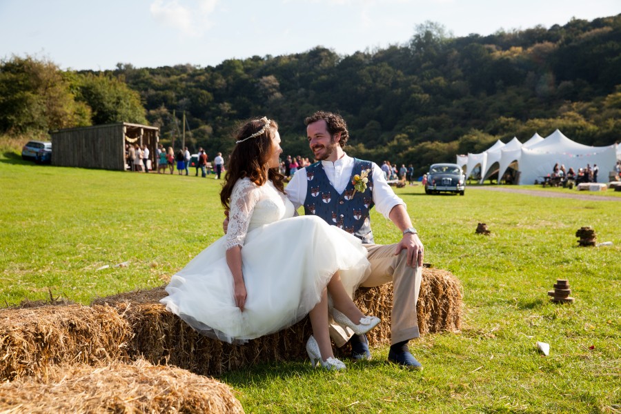 Bride and groom sitting on a hay bale in a field