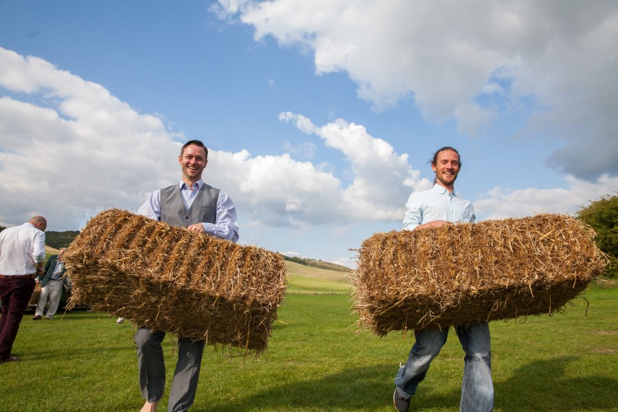 Two men smiling and carrying haybales
