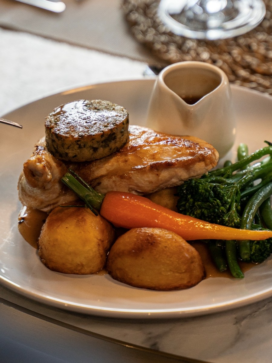 A roast meal with chicken, carrots, potatoes and a small gravy boat