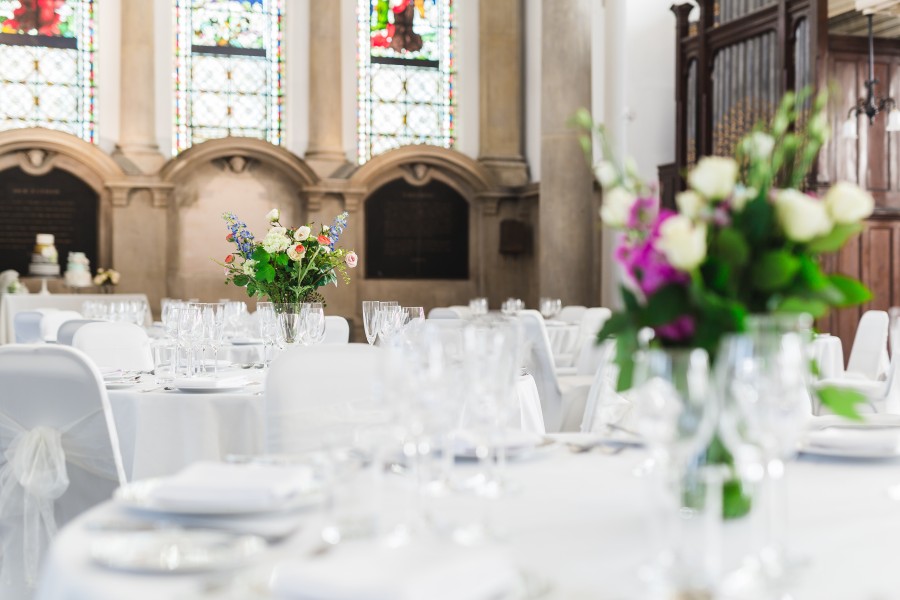 Round tables dressed for a wedding with vases of flowers, wine glasses, silver cutlery and white plates