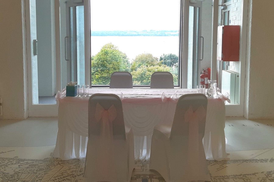 Room with a table and chairs in front of a large window overlooking the water