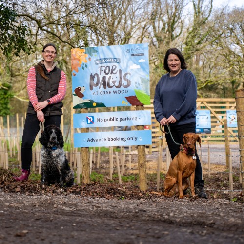 Two people stand with their dogs next to a sign that reads For Paws.