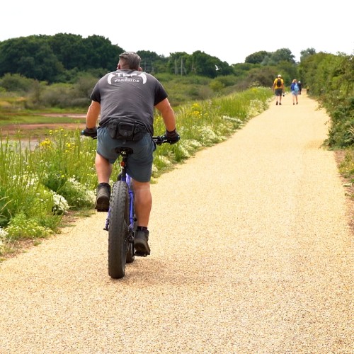 A man rides a bicycle down a path with two people walking ahead