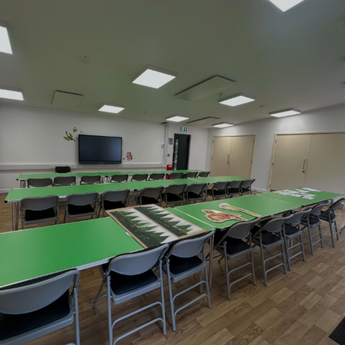 Interior look at the new outdoor classroom at Runways End, showing tables and chairs set up in front of a digital TV screen.