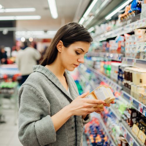 woman in supermarket looking at information on set of four desserts