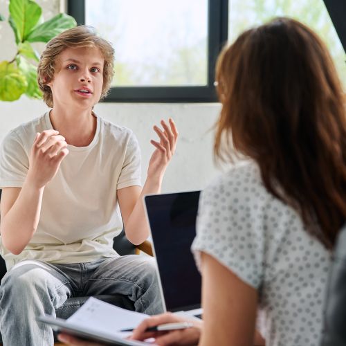 Young person talking to a woman who is facing away from camera