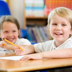 A young girl and boy sat at school desk smiling