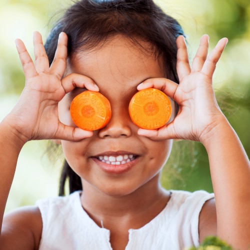 child holding carrot slices up to her eyes