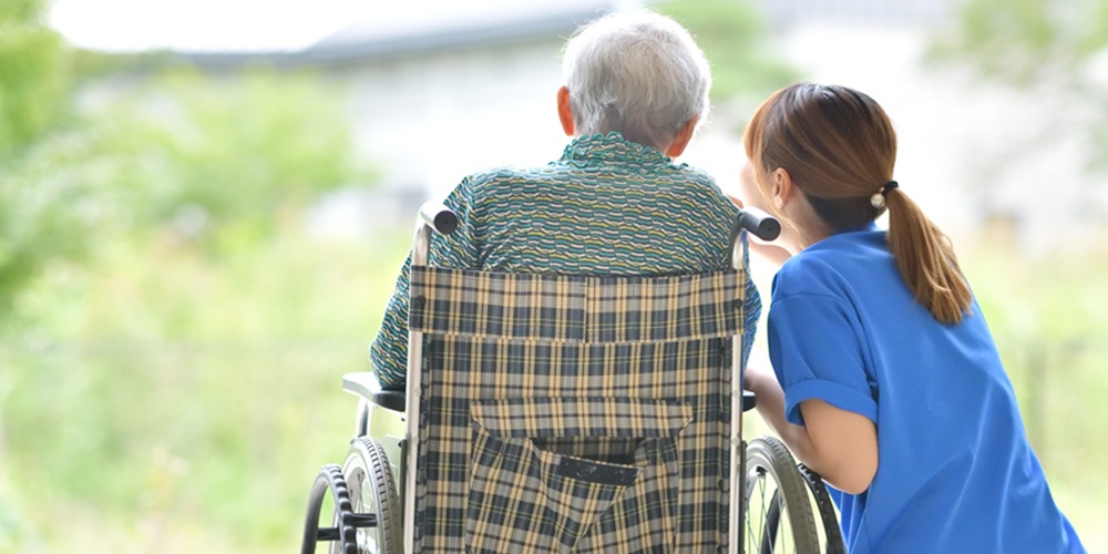 Back of elderly man in a wheelchair with nurse beside him