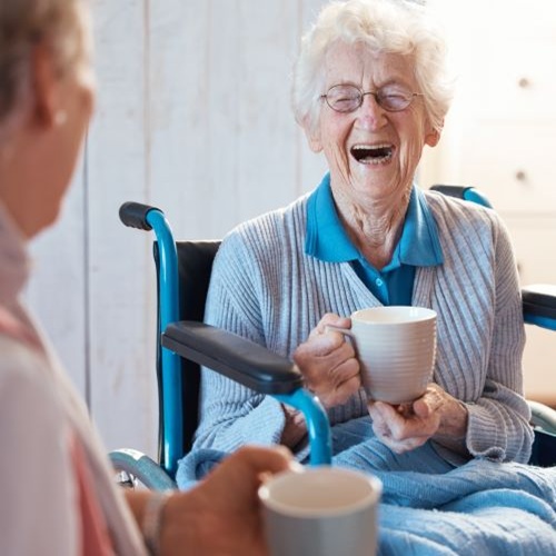 Two older ladies chatting and smiling in a care setting