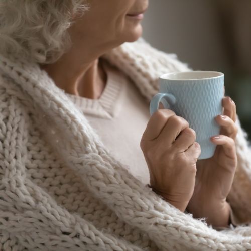 woman looking cosy and warm wrapped in a blanket with a hot drink