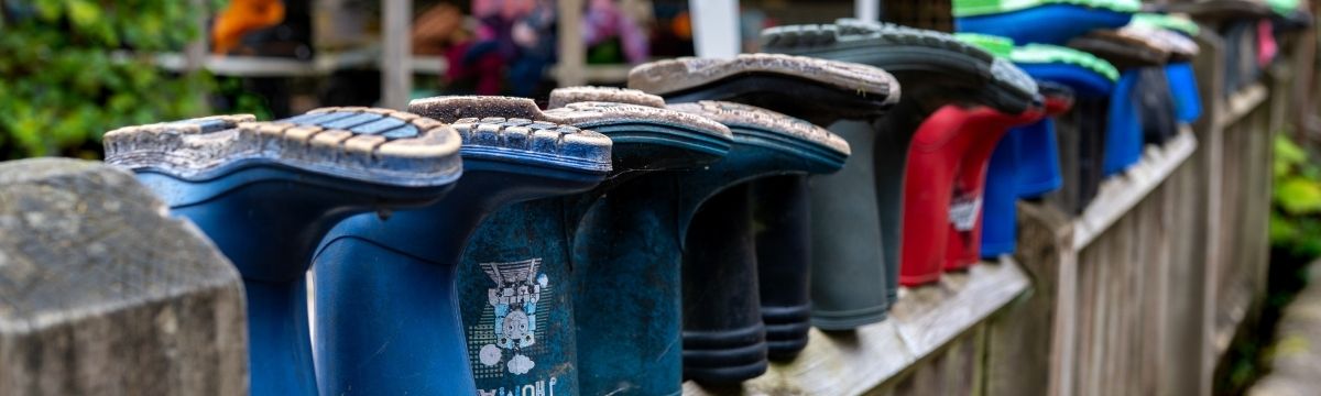 A row of colourful wellington boots lined upside down along a wooden fence at an outdoor setting