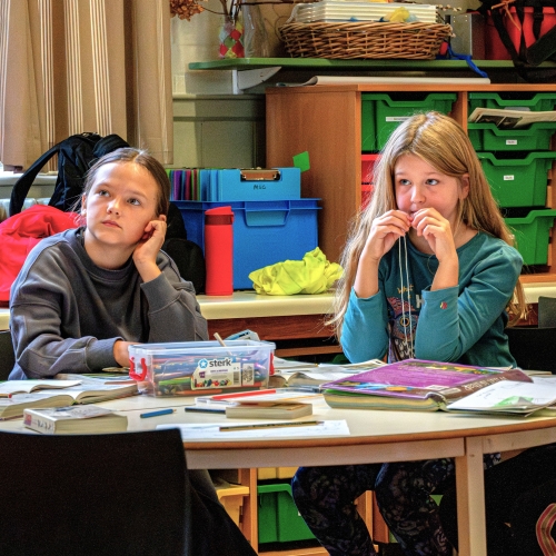 School-age children in a classroom with a box of crayons, books and colouring sheets
