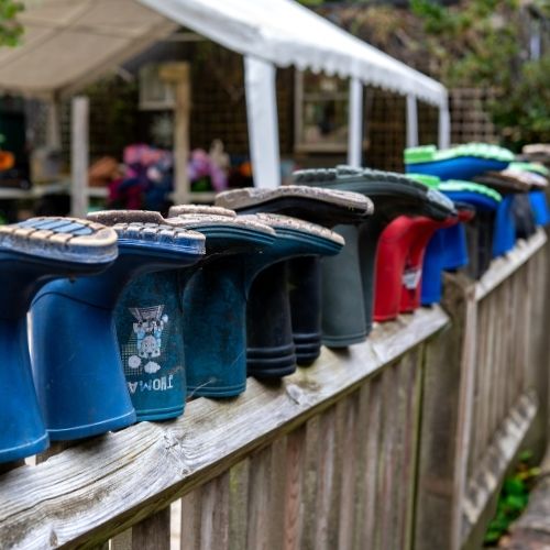 A row of colourful wellington boots lined upside down along a wooden fence at an outdoor setting
