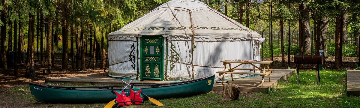 A yurt in the forest at Runway's End, with a canoe and picnic bench in front