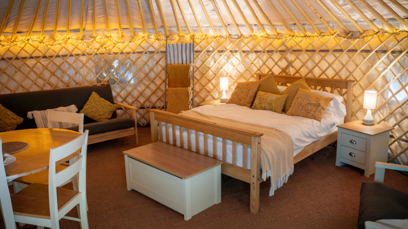 The interior of a yurt, with a bed, sofa, storage, and cosy fairylights