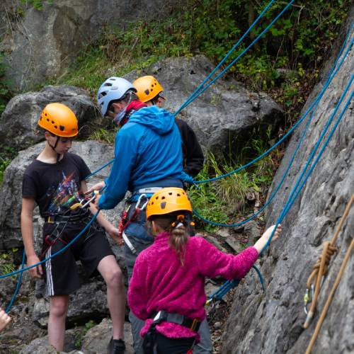 Boy in a hard hat and harness climbing up a rope attached to a cliff face