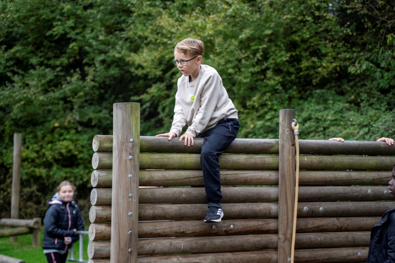 Boy climbing over a wooden obstacle as part of a course