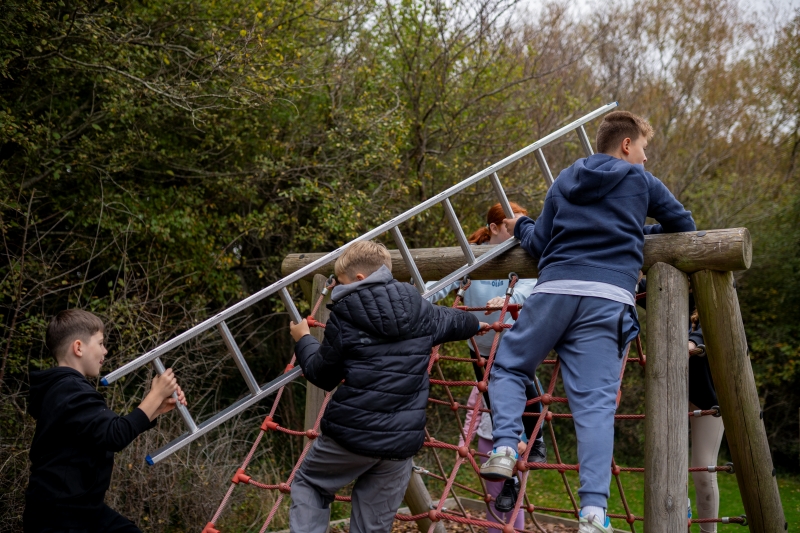 Children ding a teamwork activity carrying a ladder over an obstacle course
