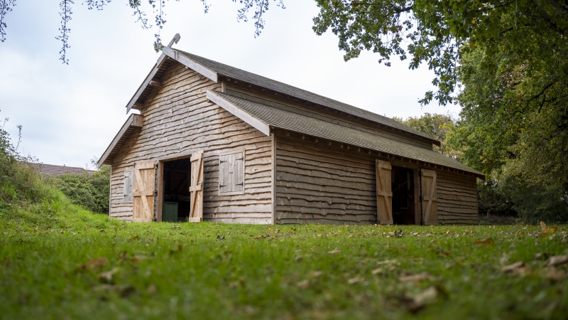 Barn building with wide open doors among lush grass and green trees