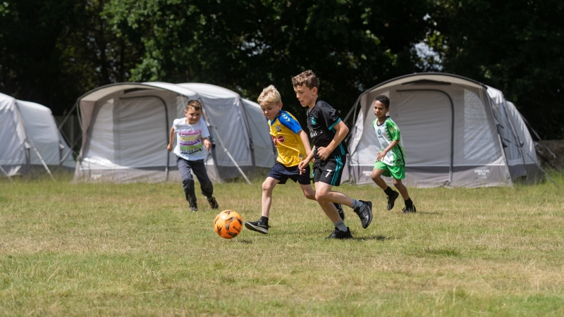 Children playing football in a camping field with tents in the background