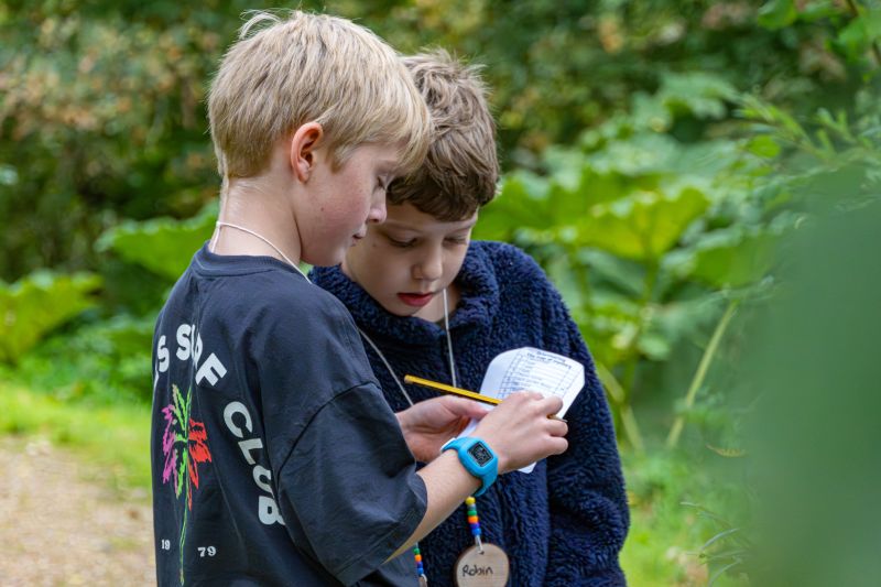Two children in a woodland setting marking items off a checklist