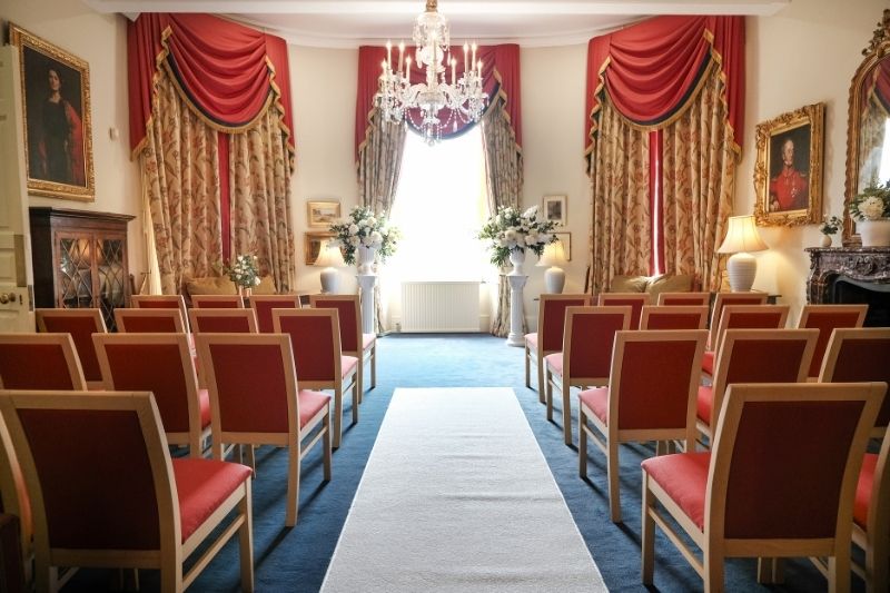 Wedding ceremony setup at Serle's House featuring a white aisle runner, red guest seating, elegant floral arrangements and a crystal chandelier.