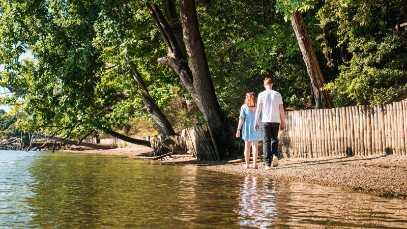 Couple walking alongside the river under the trees