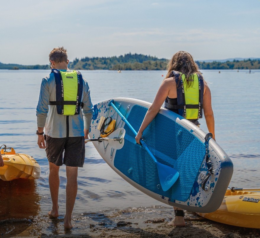 Two people with a paddleboard looking out to sea.
