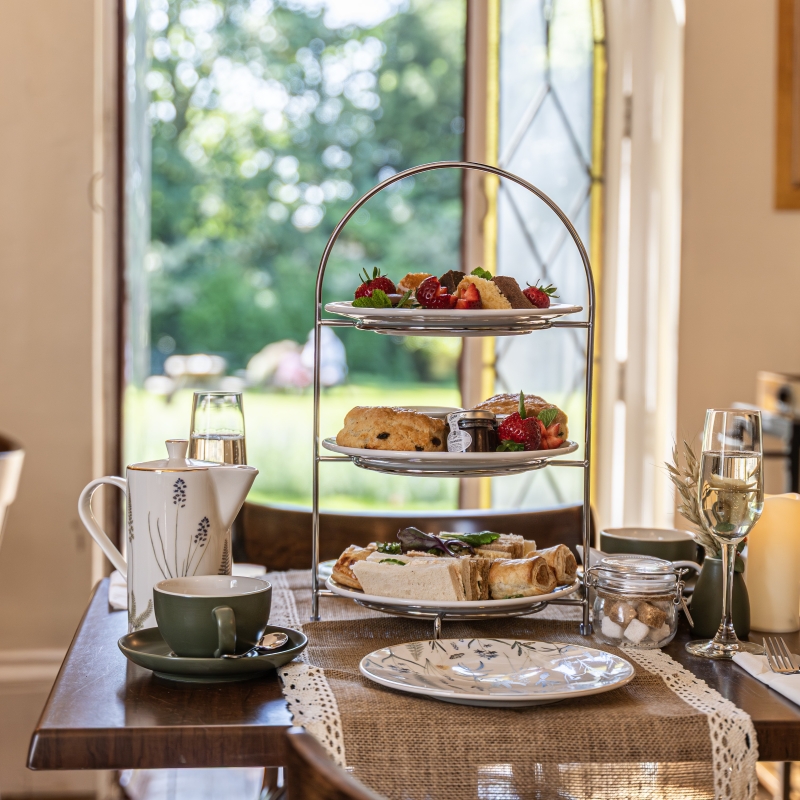 A tiered cake stand on a table in front of an open door that leads to a sunny garden.