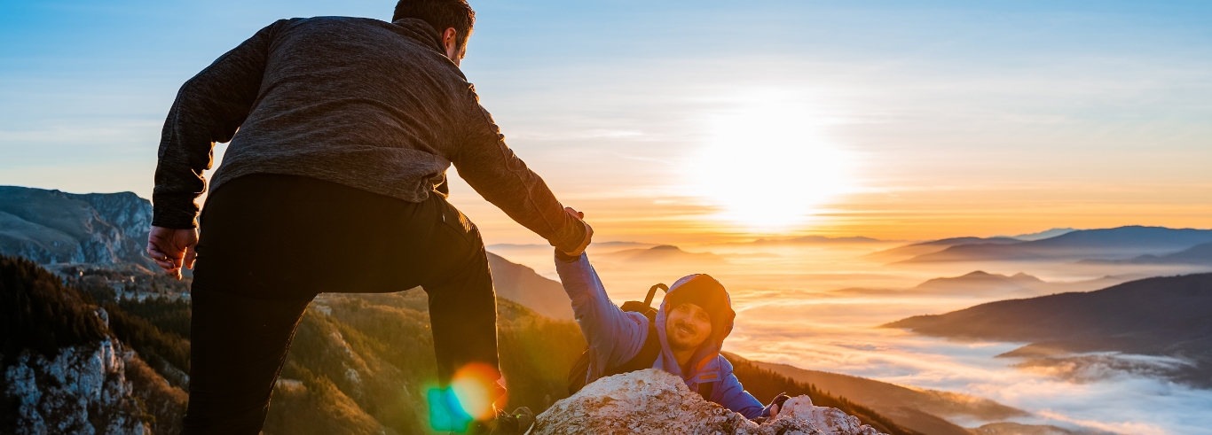 Two men helping each other whilst climbing
